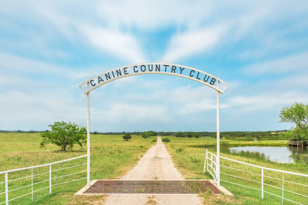 The Canine Country Club ranch gate on a gravel road between open fields